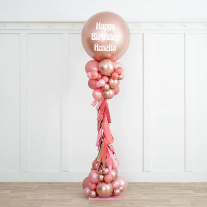 Rose gold and blush pink personalized birthday balloon pillar with Happy Birthday Amelia text