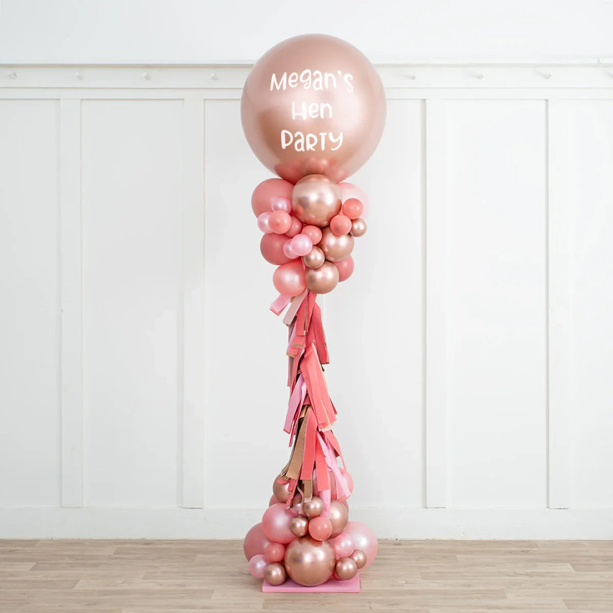 Rose gold and blush balloon pillar with personalized text Megan's Hen Party in a white room