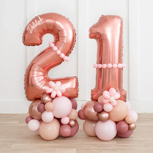 Rose gold inflated number 21 balloon stack with pink and beige balloon bouquets on wooden floor