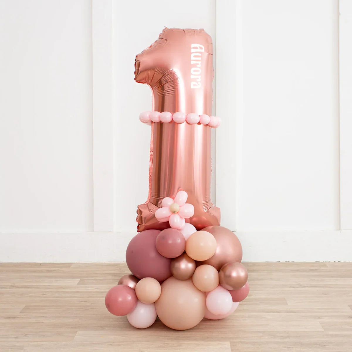 Rose gold number 1 balloon decorated with pink and beige balloon cluster on wooden floor