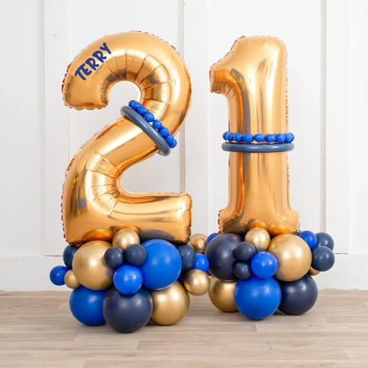 Gold foil number 21 balloons with blue and gold balloon clusters on wooden floor against white wall