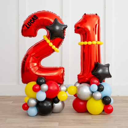 Red number 21 foil balloons with black stars, yellow bead accents, and multicolored balloon bases on wooden floor