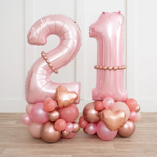 Personalized rose gold 21 number balloons with blush and metallic balloon clusters on wooden floor
