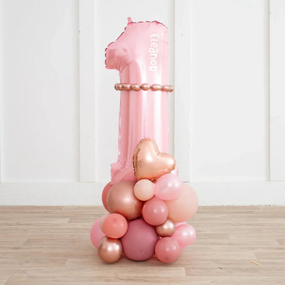 Personalized rose gold blush pink number 1 balloon stack with heart-shaped balloon on wooden floor