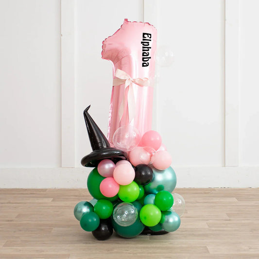 Personalized pink number 1 balloon with Elphaba text and witch hat balloon stack with green, pink, and black balloons