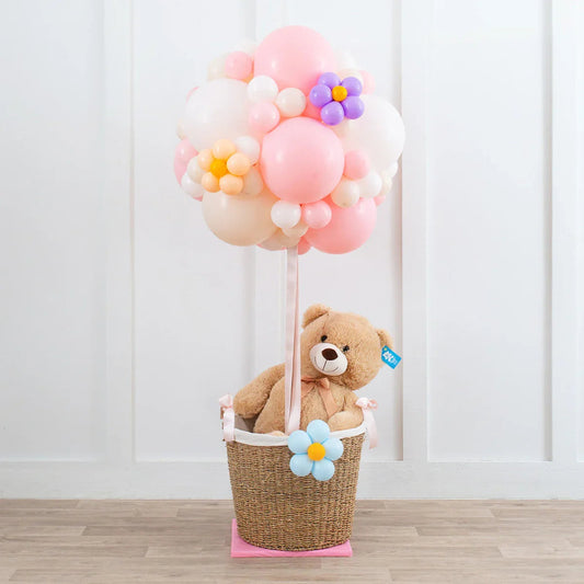 Teddy bear in basket with pastel pink and white balloon bouquet decorated with balloon flowers