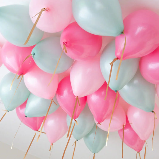 Cluster of pink, mint, and light blue helium balloons with gold ribbons floating on a white ceiling