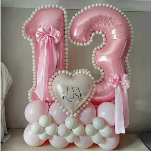 Pink number 13 balloon arrangement with white pom-pom trim, bows, and heart balloon saying Eva Rose