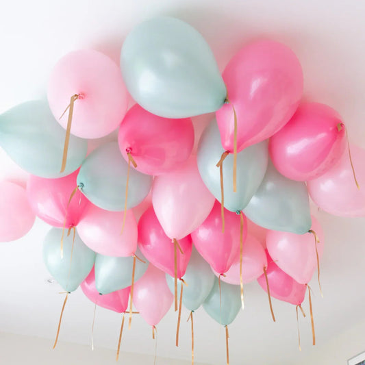 Helium-filled pink and mint balloons clustered on a white ceiling with gold ribbons
