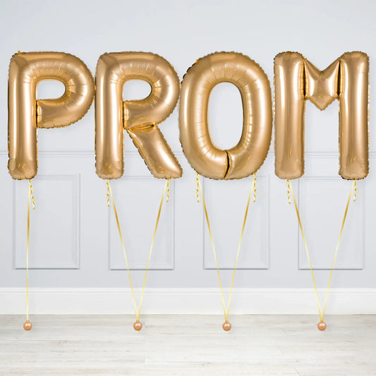 Gold foil helium balloons spelling PROM against white paneled wall on light floor