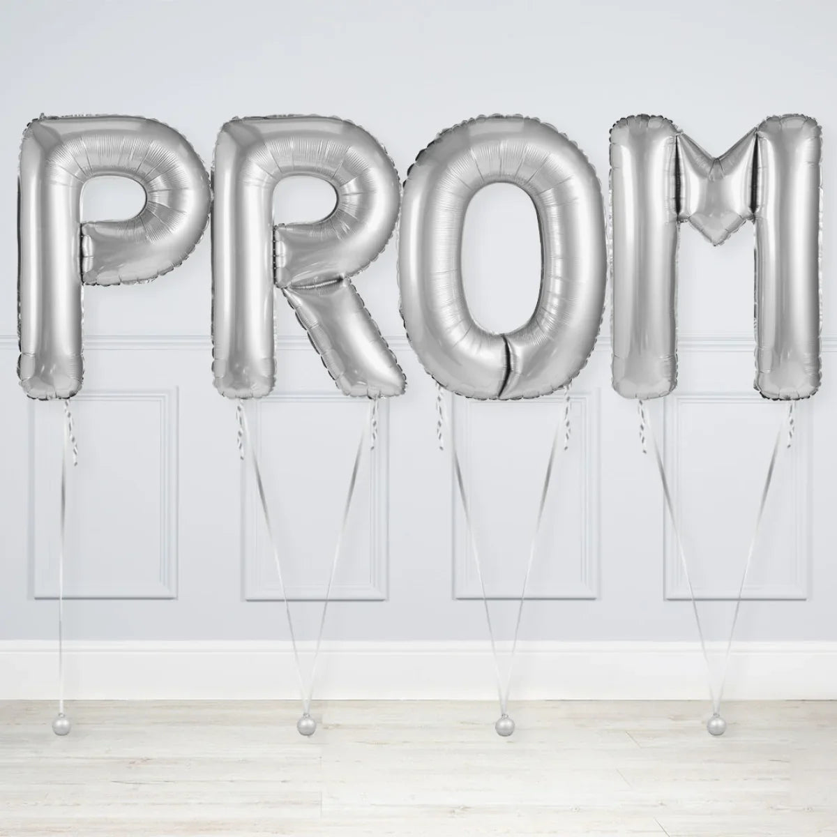 Silver foil balloons spelling PROM against a light gray wall and wooden floor