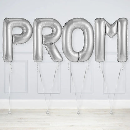 Silver foil balloons spelling PROM against a light gray wall and wooden floor