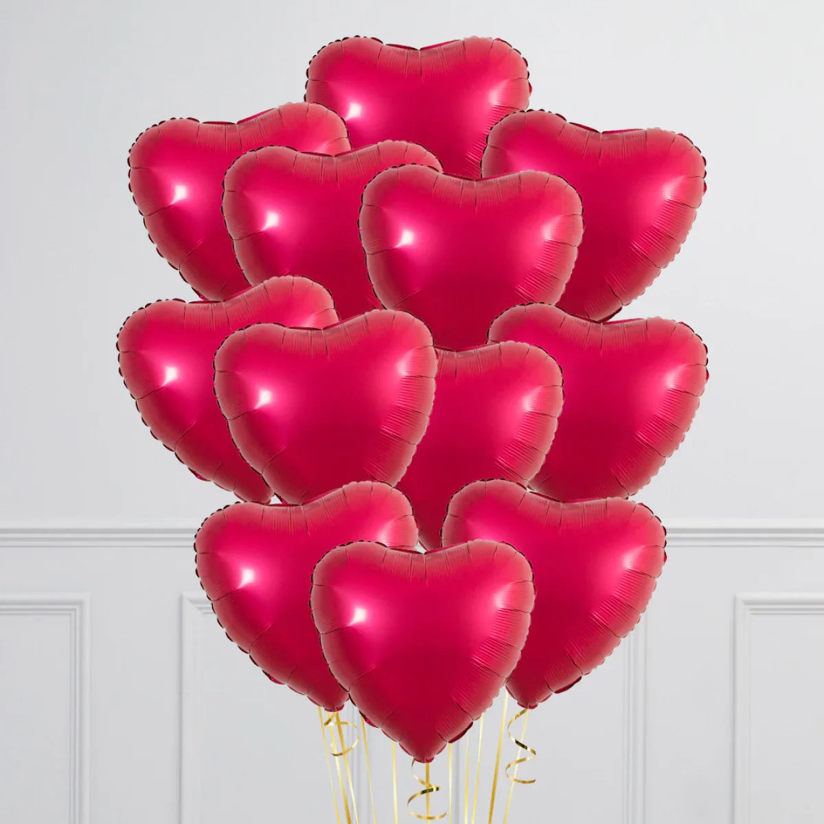 Cluster of red heart-shaped balloons with golden ribbons against white wall