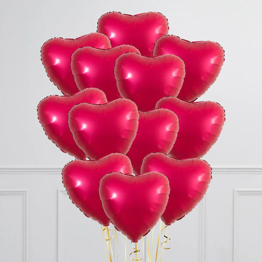 Cluster of red heart-shaped balloons with golden ribbons against white wall
