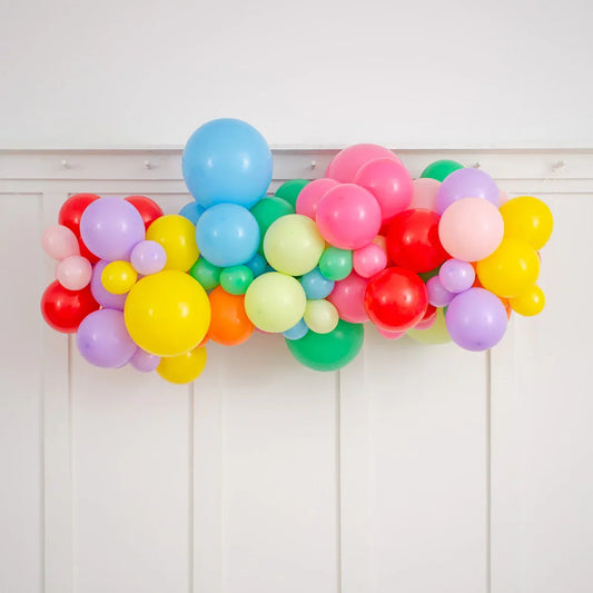 Colorful rainbow balloon garland with assorted sizes against white paneled wall