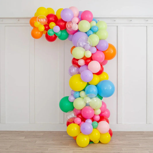Colorful balloon arch in number one shape with varied sizes and pastel shades on wooden floor