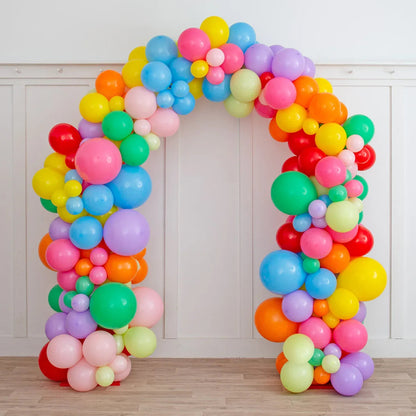 Colorful rainbow balloon arch with mixed sizes in indoor party setting on wooden floor