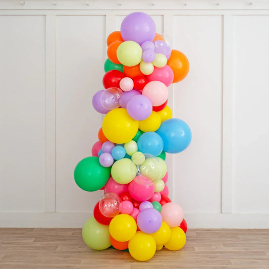 Colorful rainbow balloon pillar with various sizes and clear balloons indoors on wooden floor