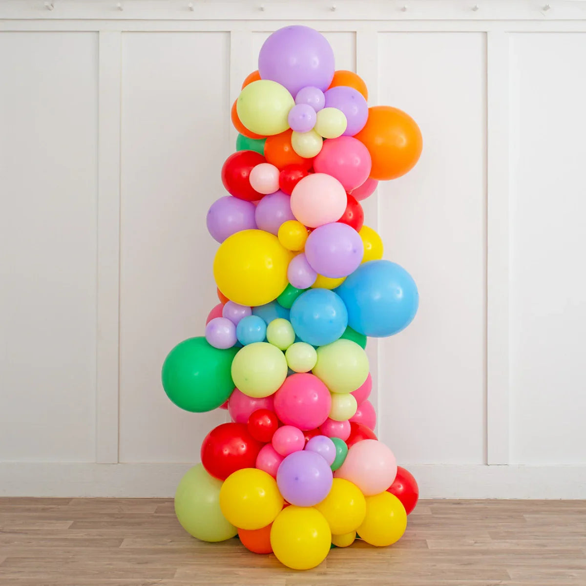 Colorful rainbow balloon pillar with various sizes in bright indoor setting on wooden floor