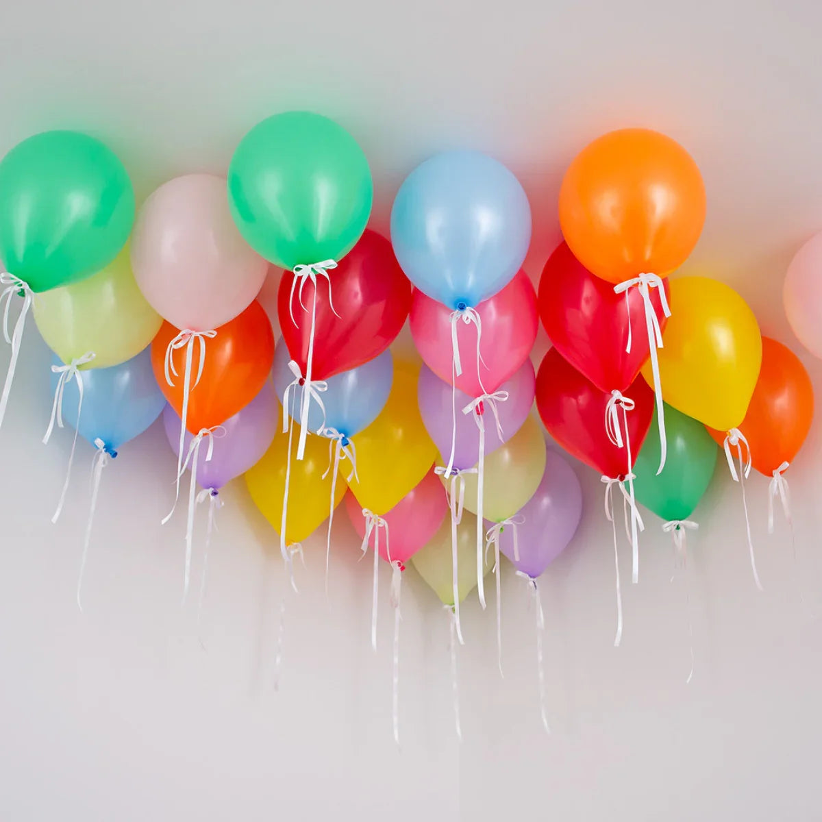 Colorful helium balloons with white ribbons floating on a white ceiling