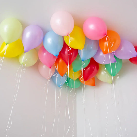 Cluster of colorful helium balloons floating near a white ceiling with curling strings