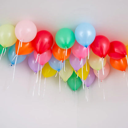 Colorful helium balloons tied with white strings floating on a white ceiling for party decoration