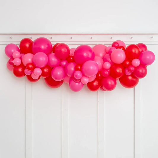 Raspberry red and pink inflated balloon garland hanging on white paneled wall