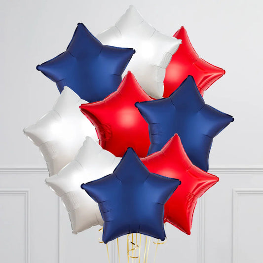 Cluster of red, white, and blue star-shaped foil balloons against a white wall background