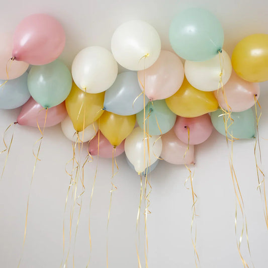 Cluster of pastel helium balloons with gold ribbons floating on a white ceiling