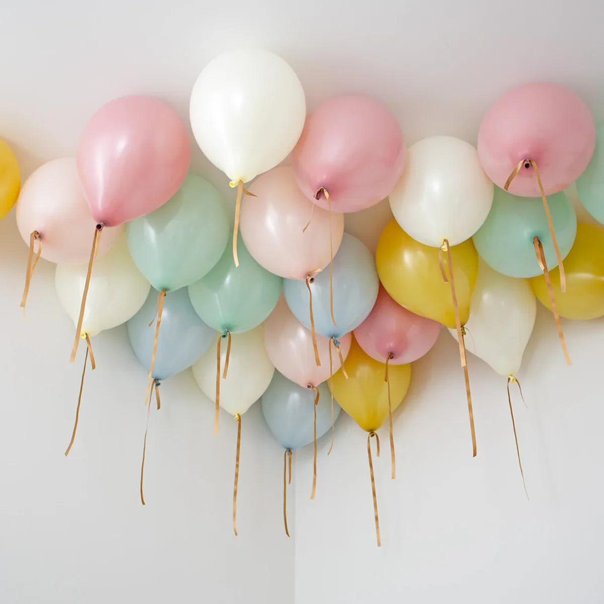 Pastel helium balloons in pink, white, yellow, blue, and green tied to ceiling with gold ribbons