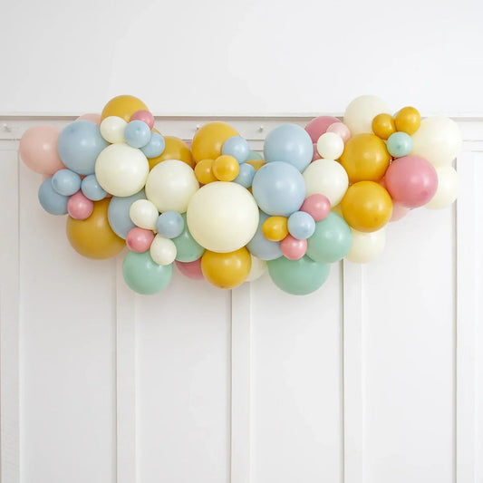 Retro pastel balloon garland with yellow, cream, pink, blue, and green balloons on white wall