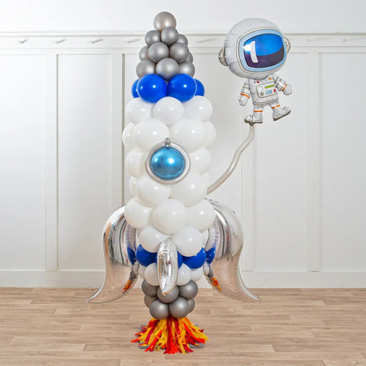 Deluxe balloon sculpture of a rocket with silver fins, flame base, and an astronaut balloon in white room