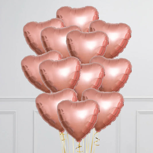 Bunch of rose gold heart-shaped foil balloons with gold ribbons indoors