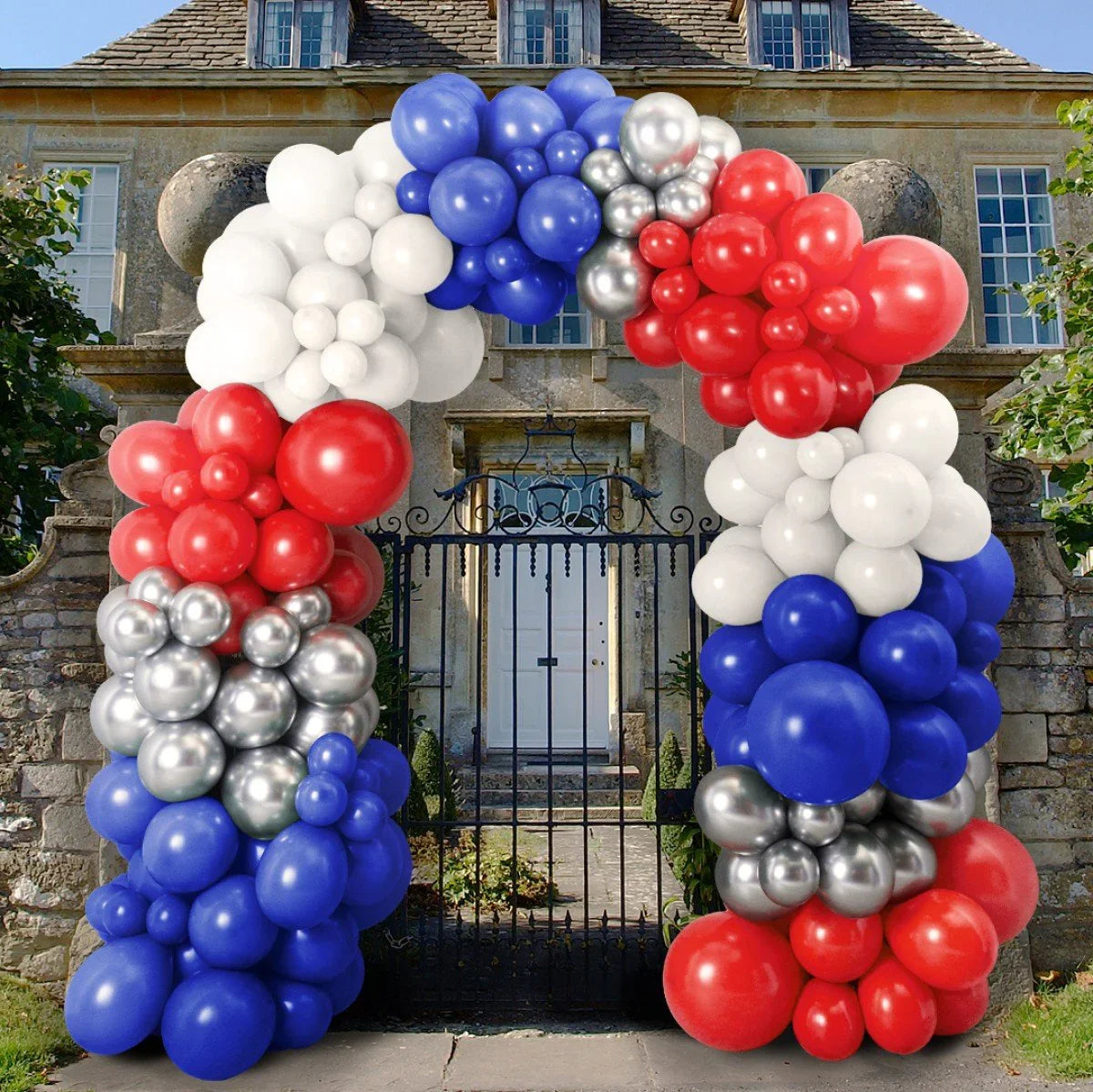 Decorative balloon arch in red, white, blue, and silver outside stone house with iron gate