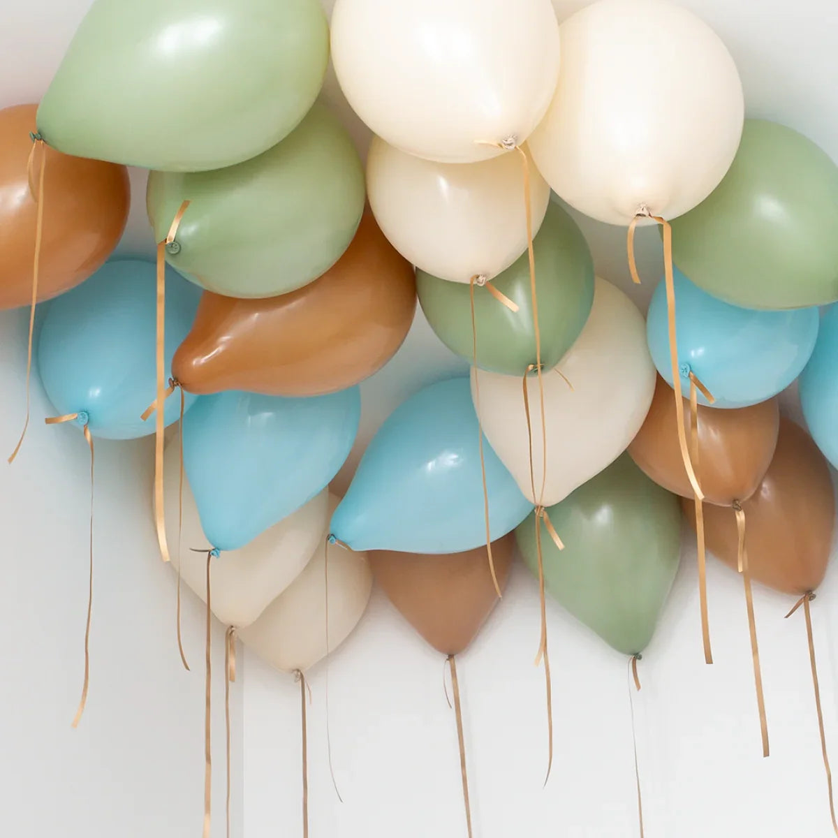 Helium ceiling balloons in pastel green, blue, cream, and brown shades with golden ribbons