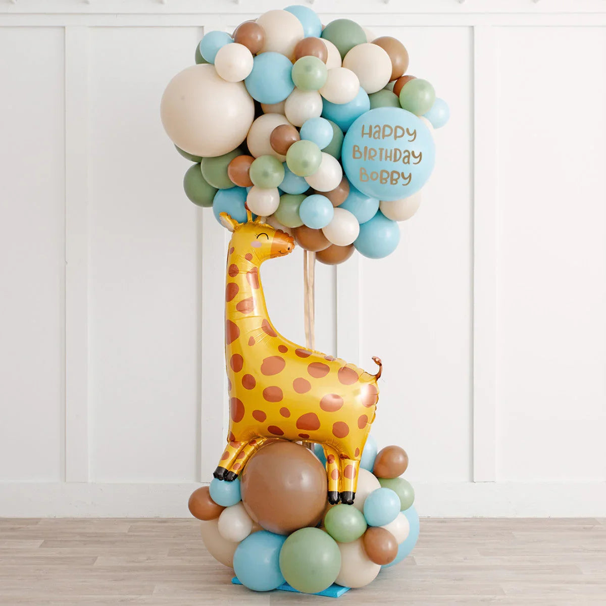 Colorful balloon arrangement with a yellow giraffe and pastel balloons, including a Happy Birthday Bobby balloon