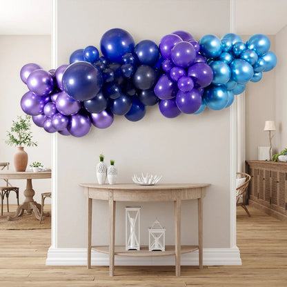 Indoor metallic blue and purple balloon garland hanging above wooden console table in modern living space