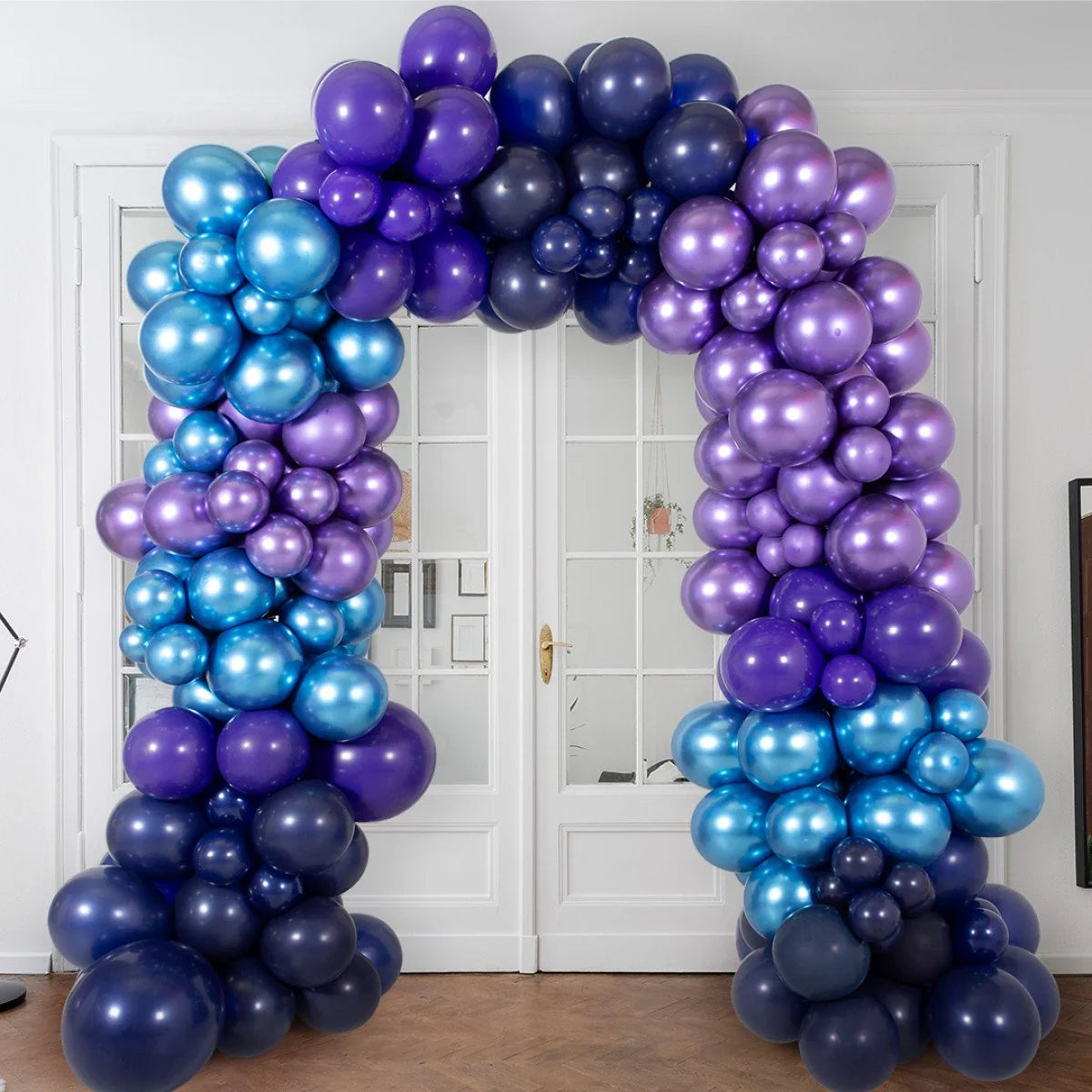 Shiny blue, purple, and navy balloon arch decorating a white double glass door in an indoor space