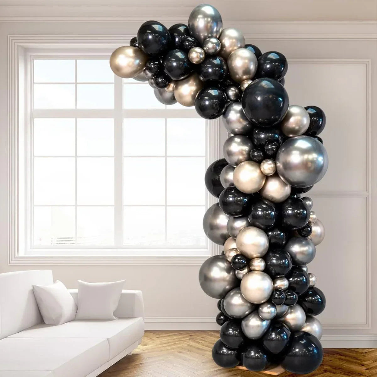 Asymmetric balloon arch with black, gold, and silver balloons in a modern white living room