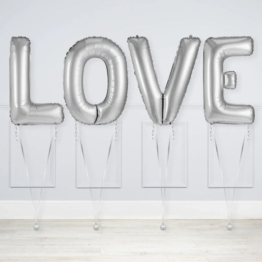 Silver foil balloons spelling LOVE inside a white room with wooden floor