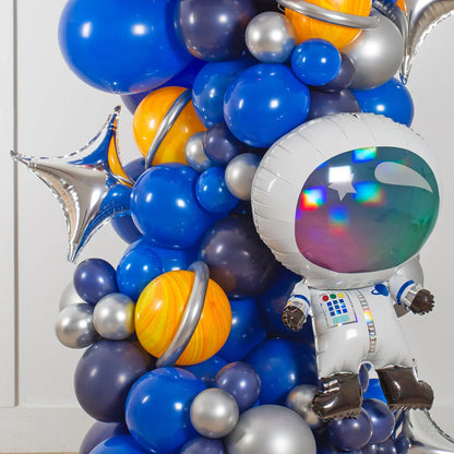 Space-themed balloon arch with blue, silver, orange planet balloons and astronaut foil balloon