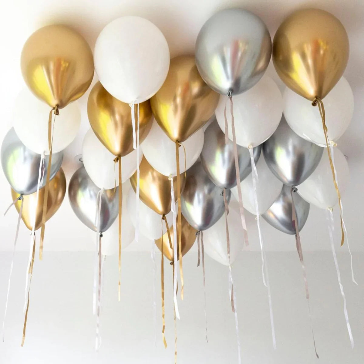 Cluster of gold, silver, and white metallic helium balloons floating on a white ceiling