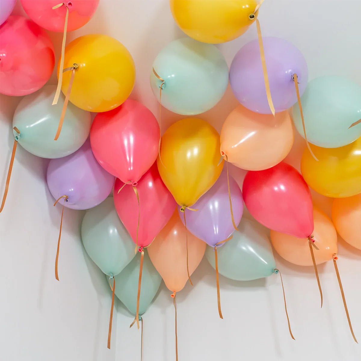Helium balloons in pastel colors including yellow, pink, purple, and mint, floating on a white ceiling corner