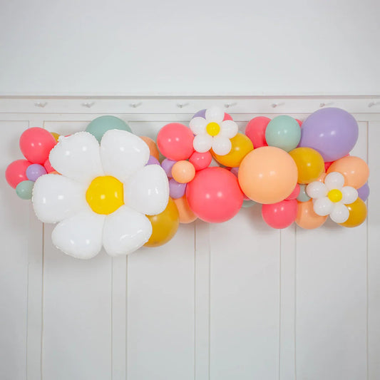 Colorful balloon garland with large white and small daisy-shaped flower balloons against white wall
