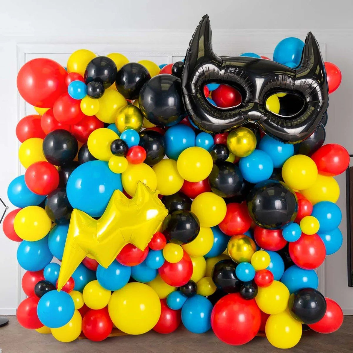 Colorful superhero-themed balloon wall with red, yellow, blue, and black balloons and Batman mask