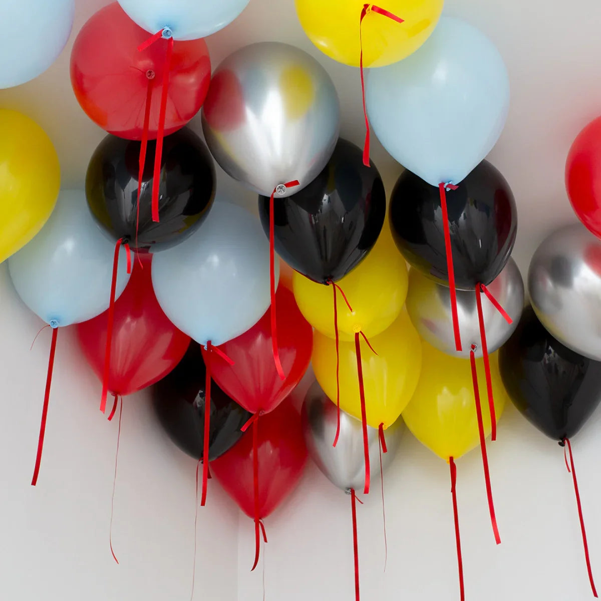 Colorful helium balloons in red, yellow, black, silver, and light blue floating near a white ceiling