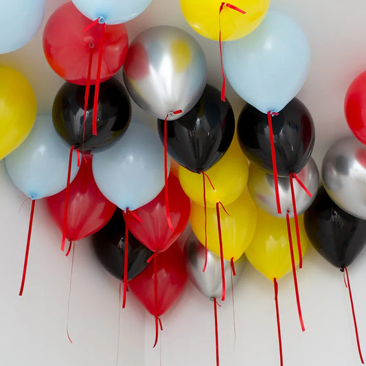 Colorful helium balloons in red, yellow, black, silver, and light blue floating near a white ceiling