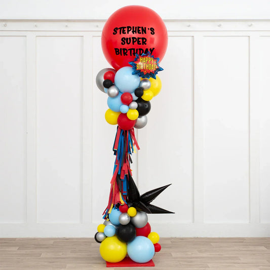 Tall colorful superhero birthday balloon pillar with red top balloon reading Stephen's Super Birthday