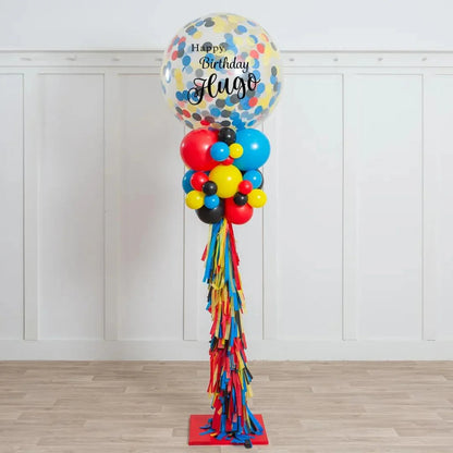 Tall birthday balloon pillar with colorful confetti balloon and red, blue, yellow, black balloons on wooden floor