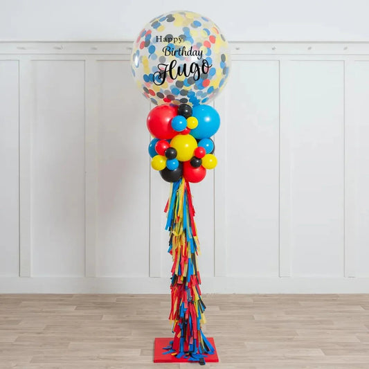 Tall birthday balloon pillar with colorful confetti balloon and red, blue, yellow, black balloons on wooden floor